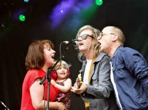 Amy Millan holding daughter Delphine while singing with Brendan Canning and Torquil Campbell.